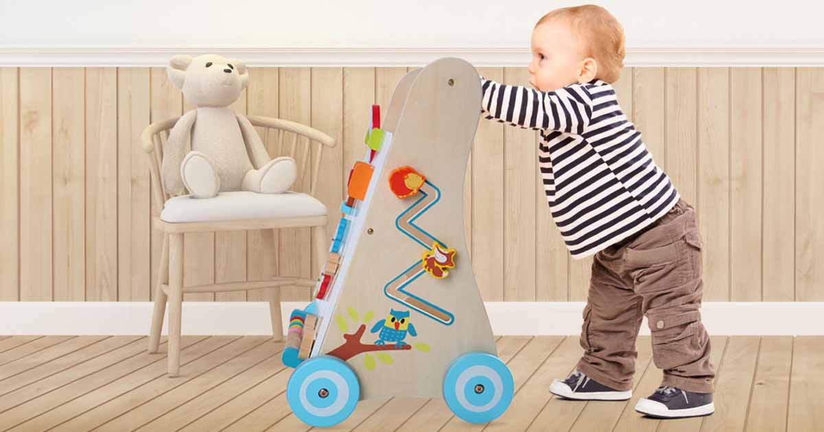 Bábätko pri prvých krokoch s dreveným chodítkom v bezpečnom domácom prostredí, ktoré podporuje rovnováhu, stabilitu a prirodzený pohyb