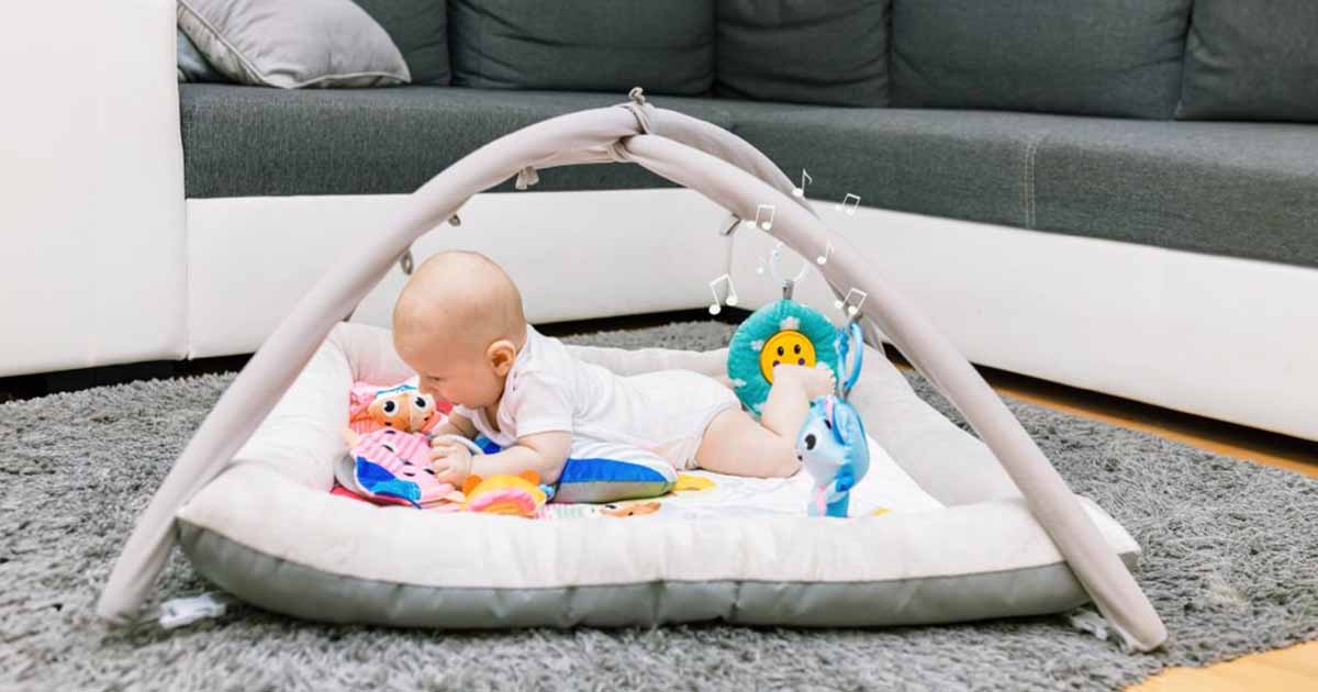 Bábätko ležiace na mäkkej hracej deke s hrazdou v bezpečnom domácom prostredí, ktoré podporuje pokojné hranie, zmyslový vývoj a pohyb od narodenia