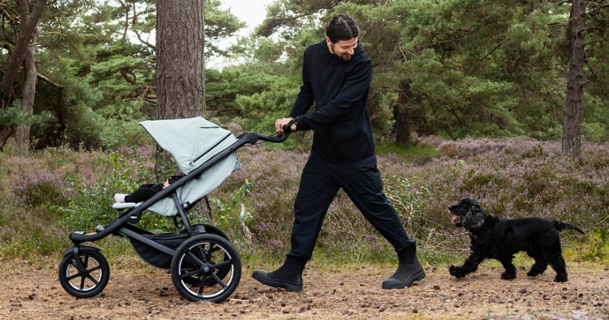 Prechádzka otca s dieťaťom v kočíku Thule Glade3 v prírode so psom.
